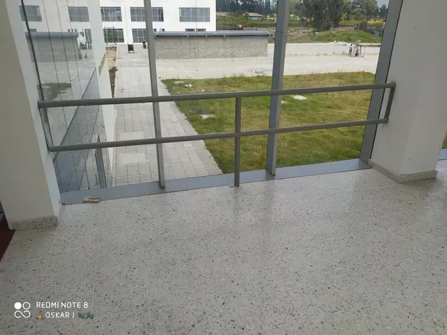 Balcón con barandilla gris que da a un patio y a un edificio moderno al otro lado.