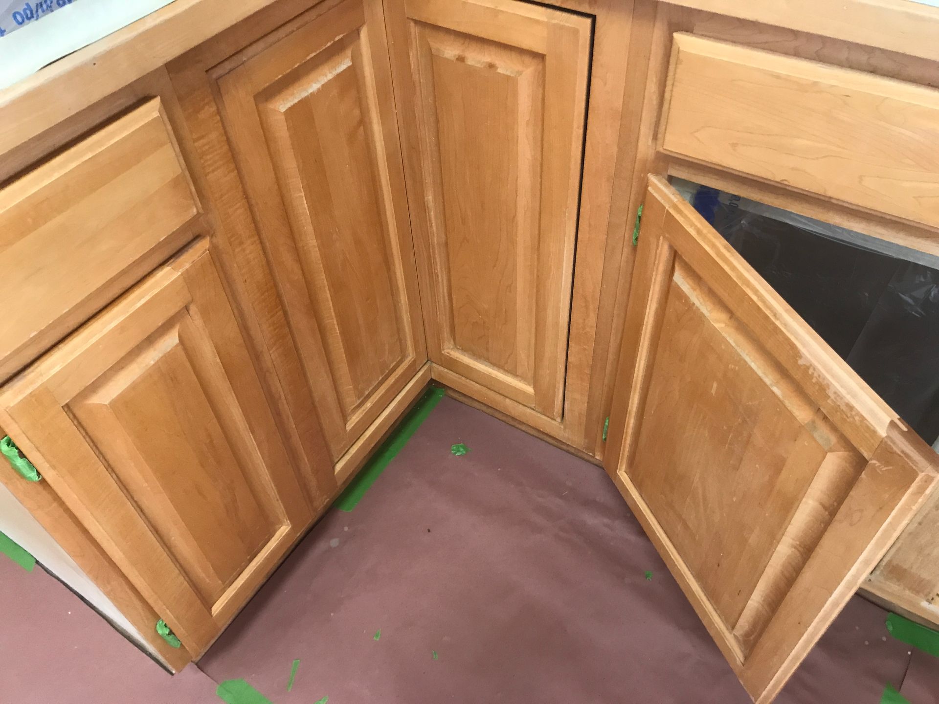 A corner kitchen cabinet assembly with light wood doors, including one slightly open door revealing the interior.