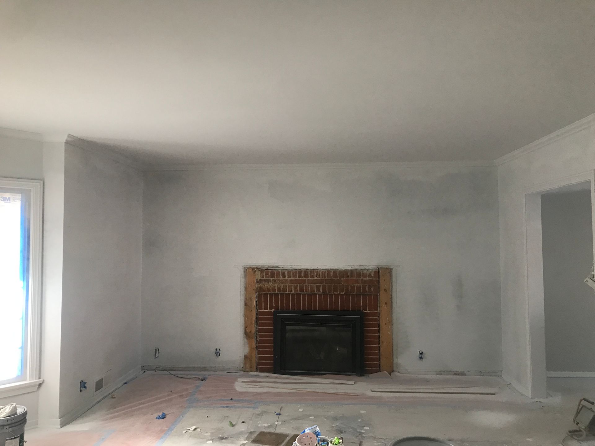 A room under renovation with light gray walls, a brick fireplace, and unfinished flooring.