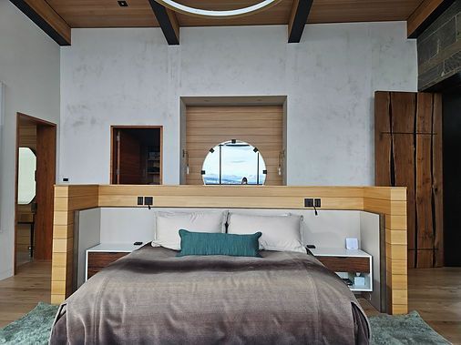A modern bedroom features a central bed with a light-wood headboard and a circular window set into a white textured wall.