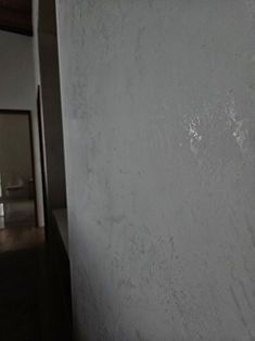 A close-up view of a textured, light gray wall surface next to a dimly lit doorway leading to a hallway.
