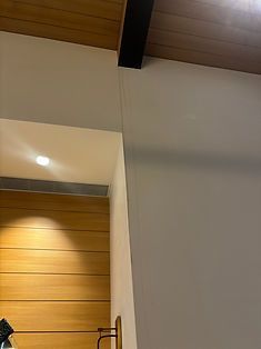 A corner view of a room with a white wall meeting a recessed area featuring horizontal wood paneling and a ceiling light.