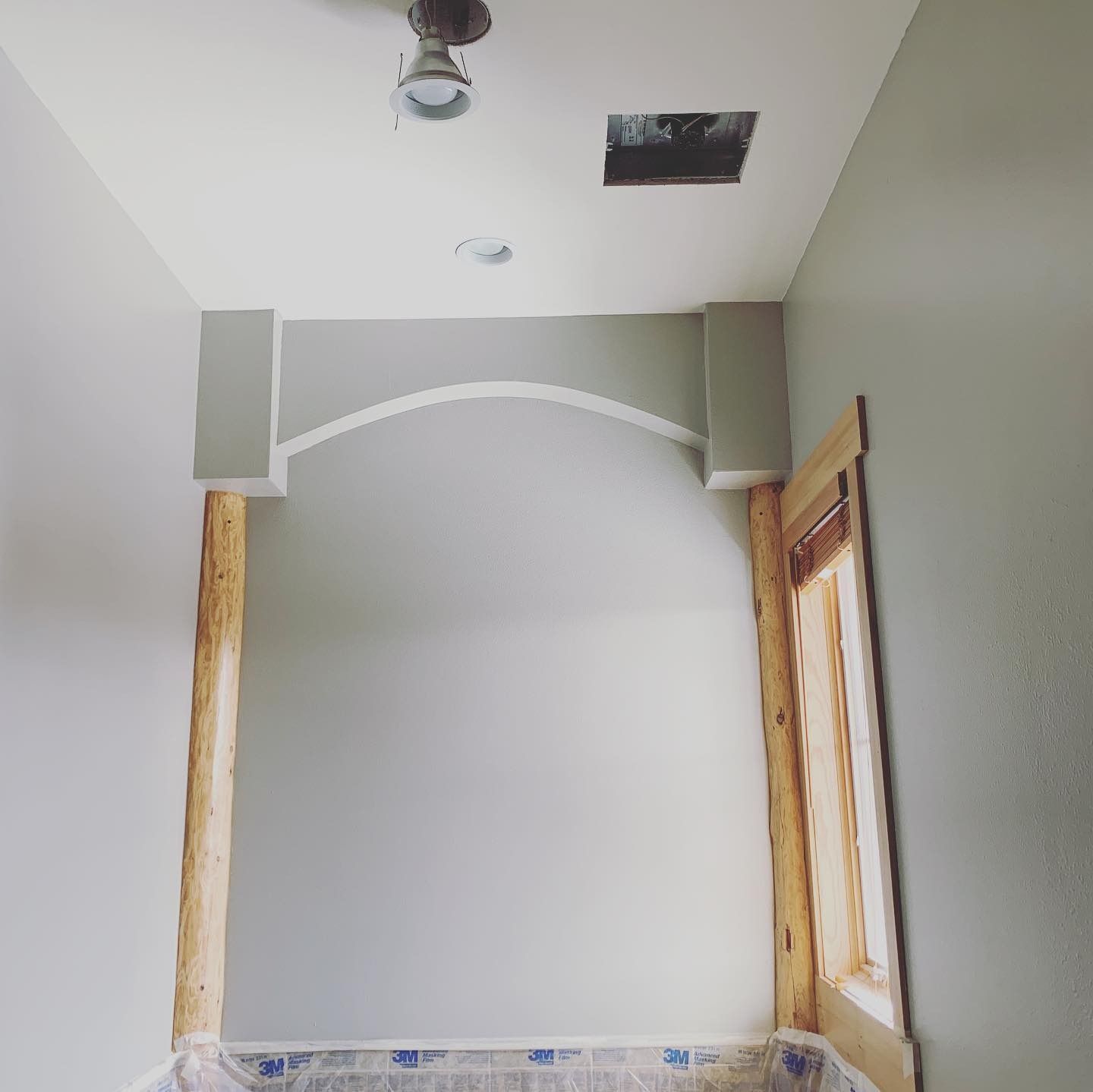 A grey arched alcove framed by rustic wooden posts under construction in a room with a light fixture and ceiling vent.