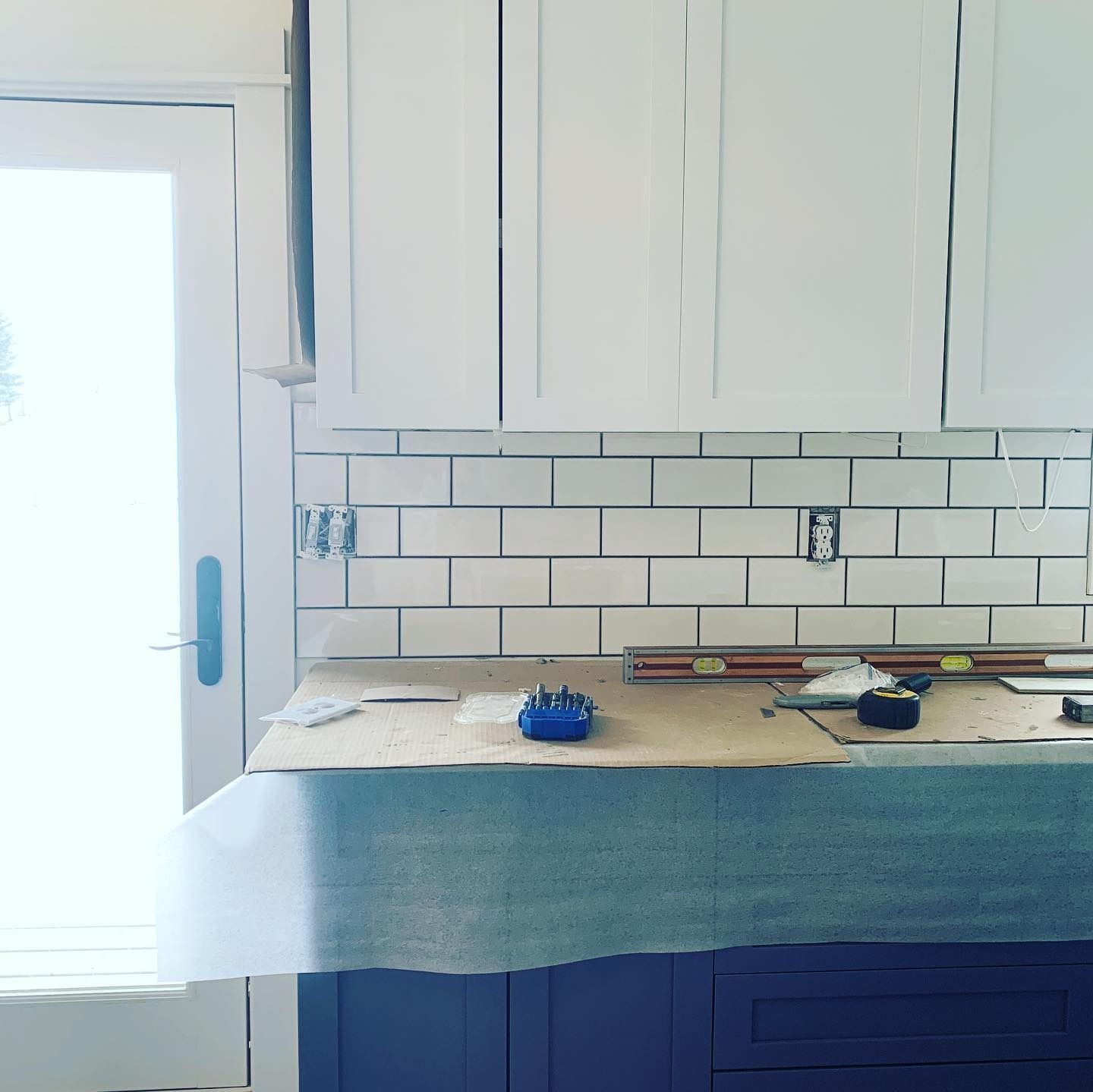 A kitchen under construction with white subway tile backsplashes, white cabinets, and blue base cabinets.