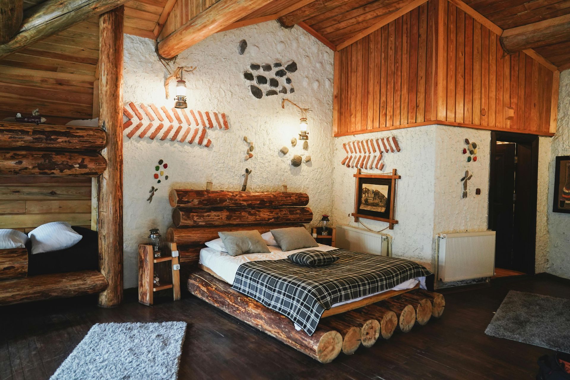 A rustic cabin bedroom featuring a bed with a log frame, wooden accents, and white plaster walls with decorative art.
