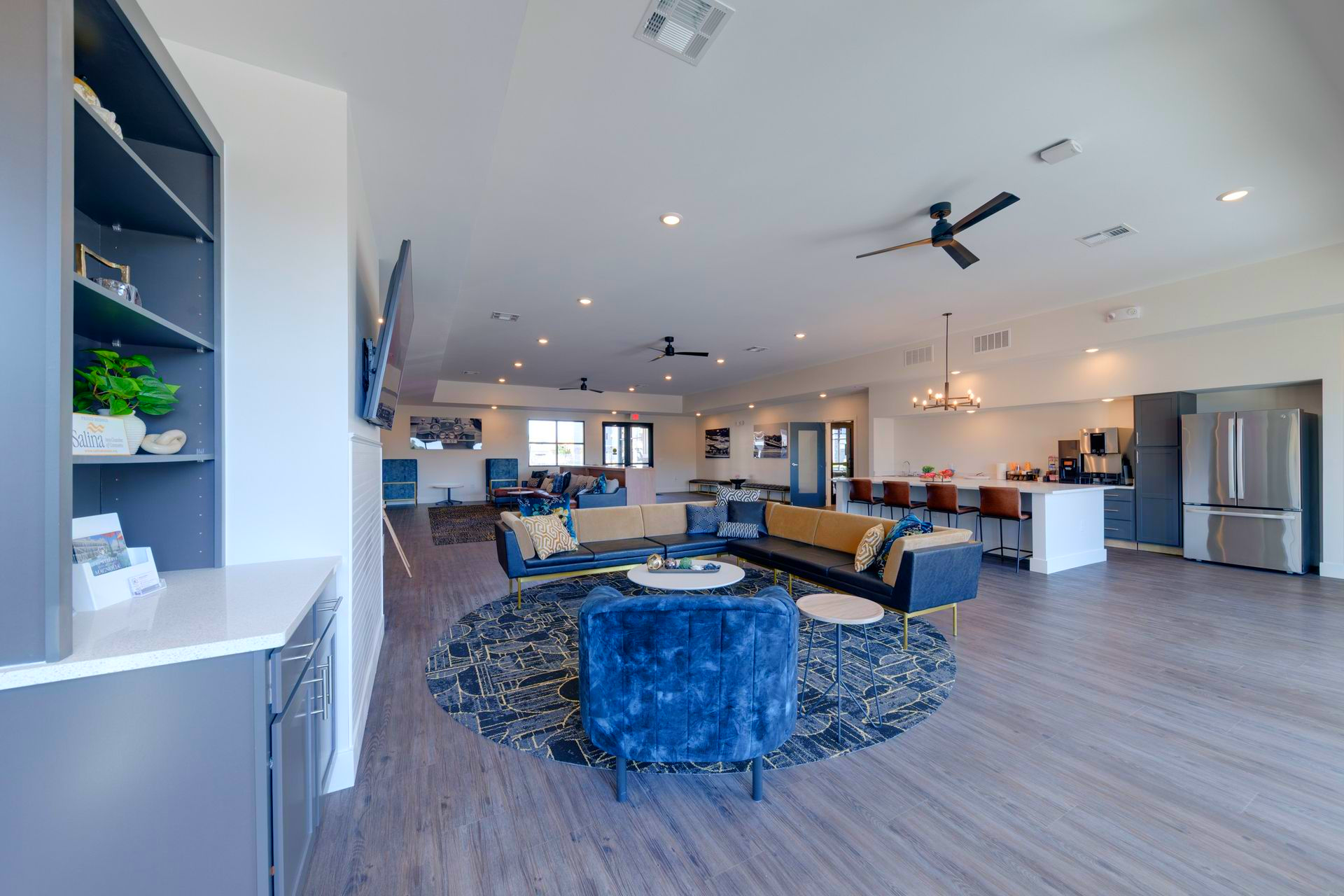 Spacious lounge with blue and gold seating, a kitchen, and built-in shelves.