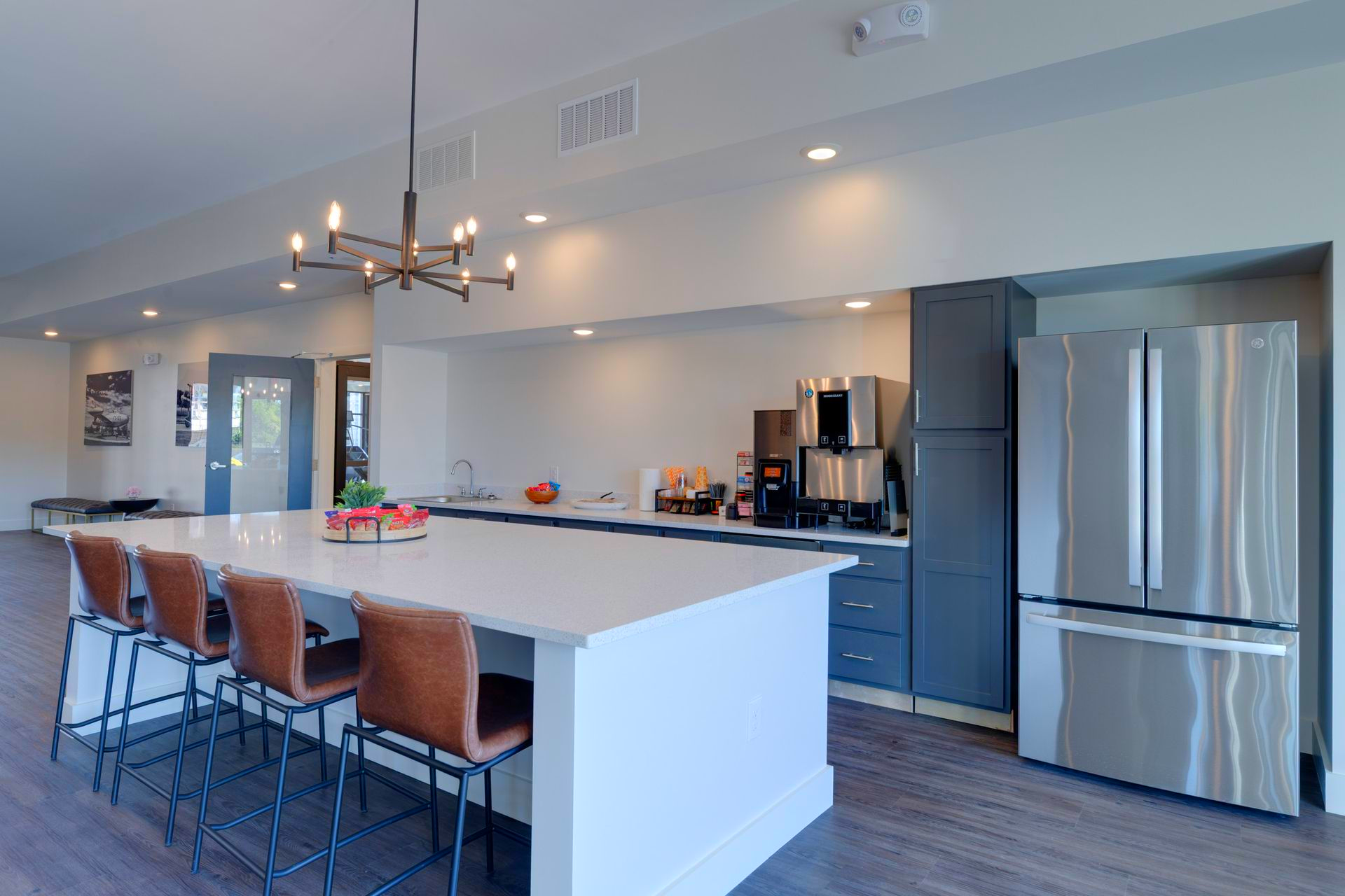 Communal kitchen with island seating, stainless steel fridge, and coffee station.