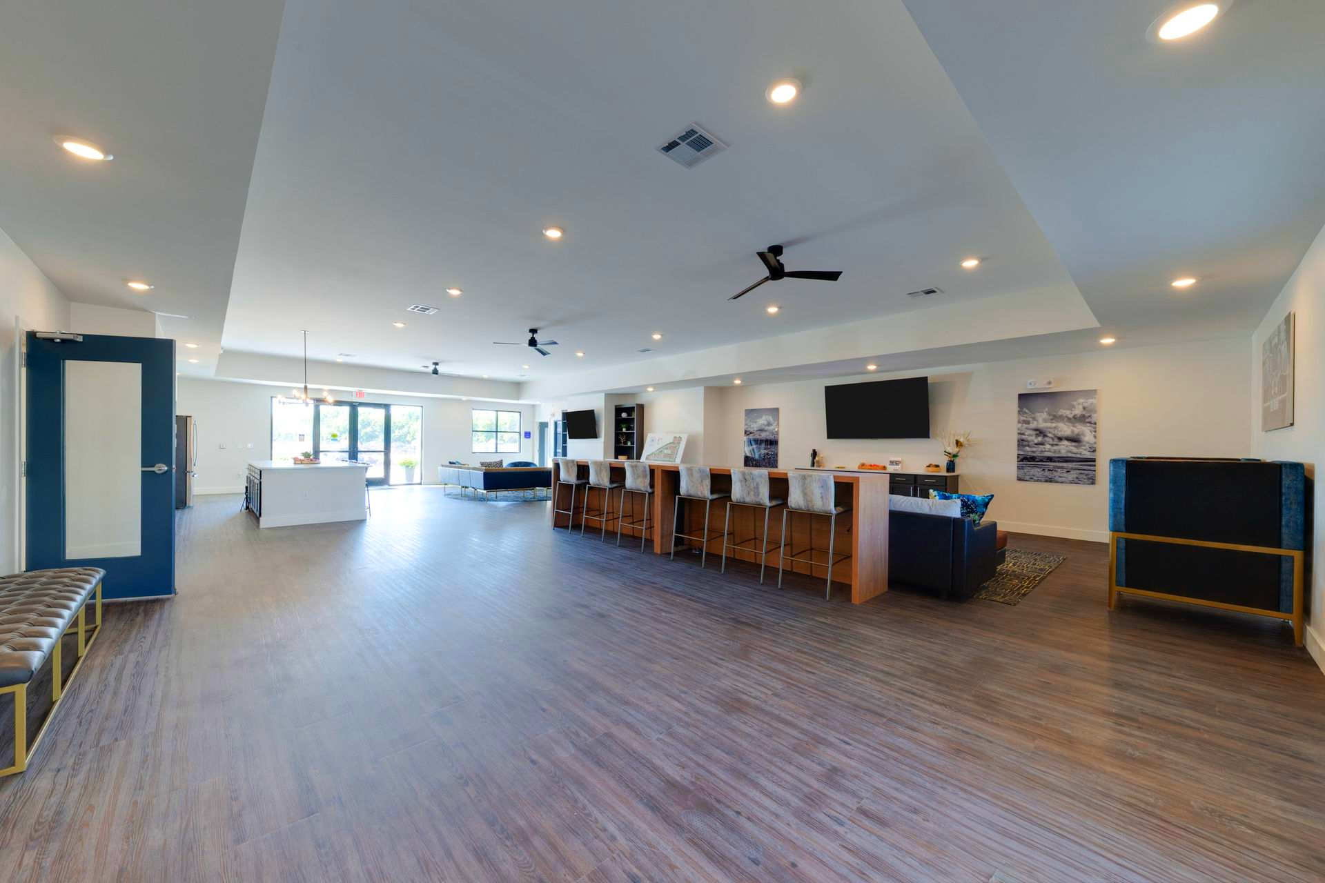 Spacious interior with a long bar, seating, and multiple TVs; neutral color palette, wood flooring.