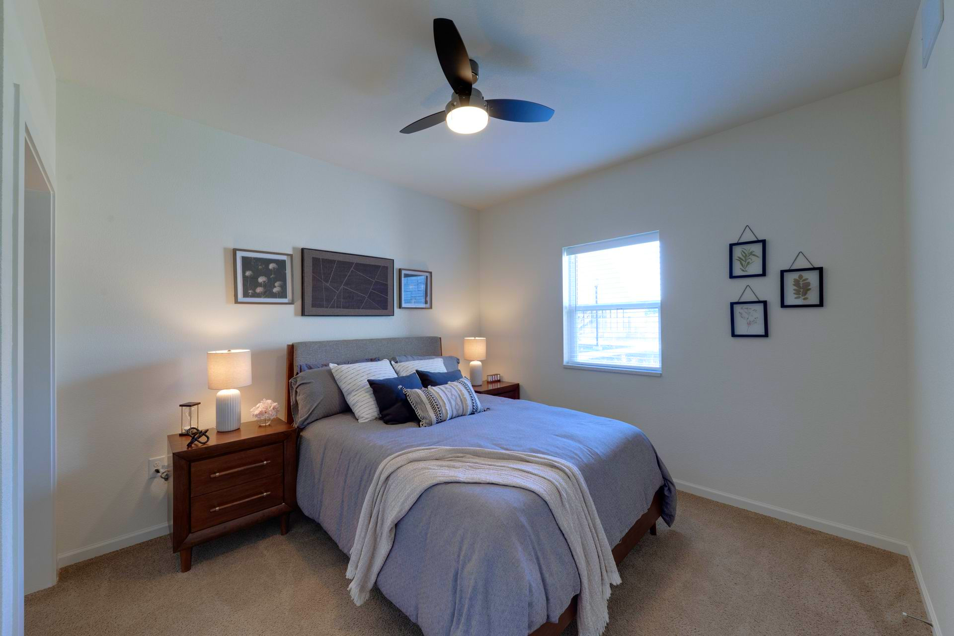 Bedroom with a bed, nightstands, lamps, and wall art. A ceiling fan is overhead.