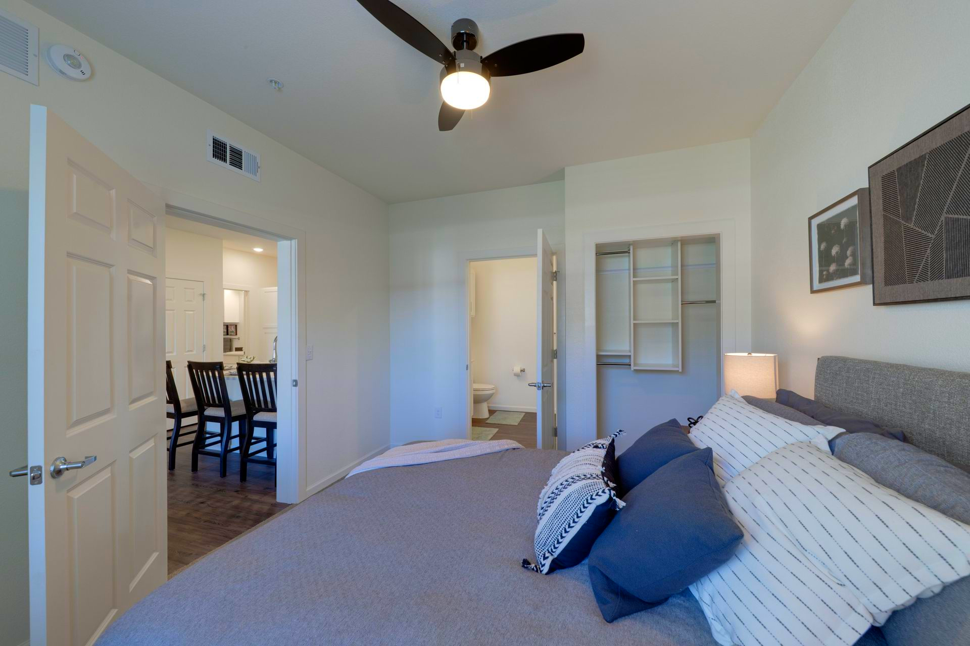 Bedroom with a bed, pillows, open doors to kitchen and bathroom, and a ceiling fan.