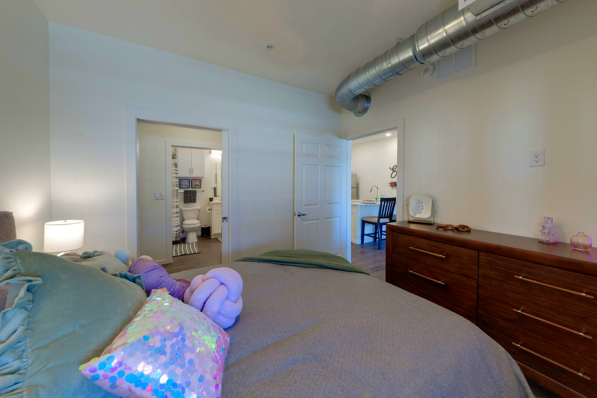 Bedroom with bed, dresser, and open doorways to bathroom and hallway.