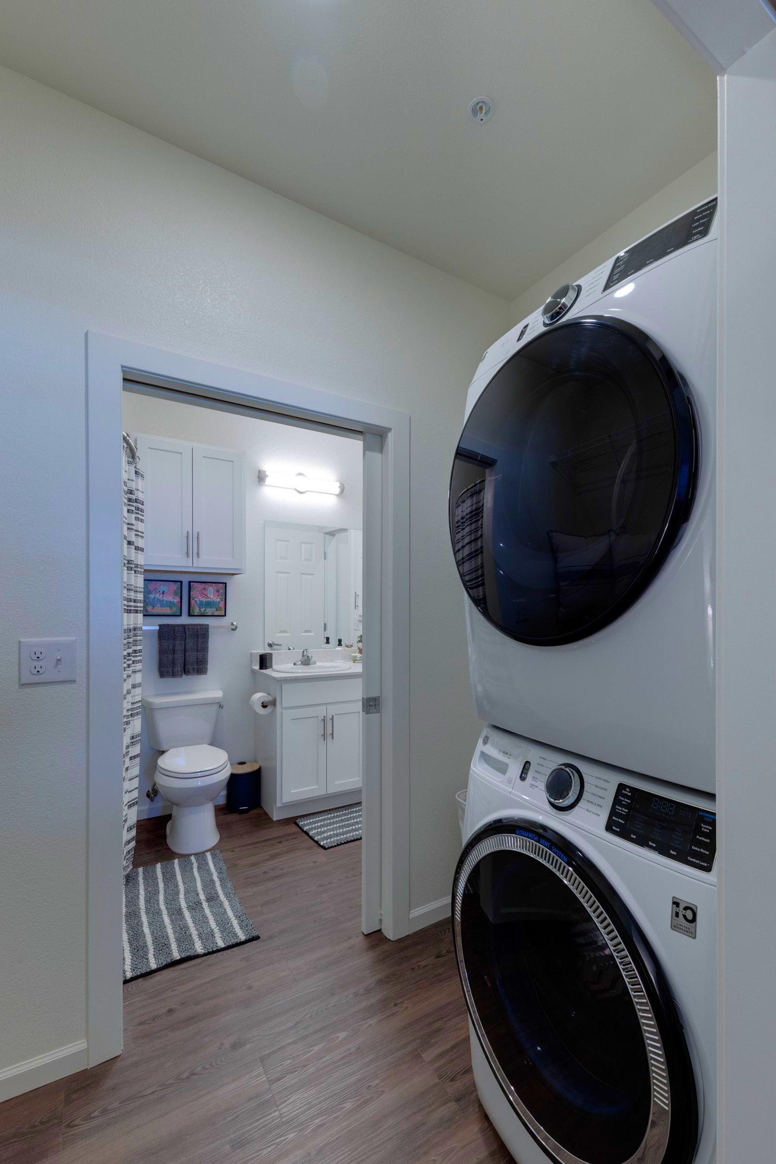 Stacked washer and dryer next to bathroom door with toilet and sink visible.