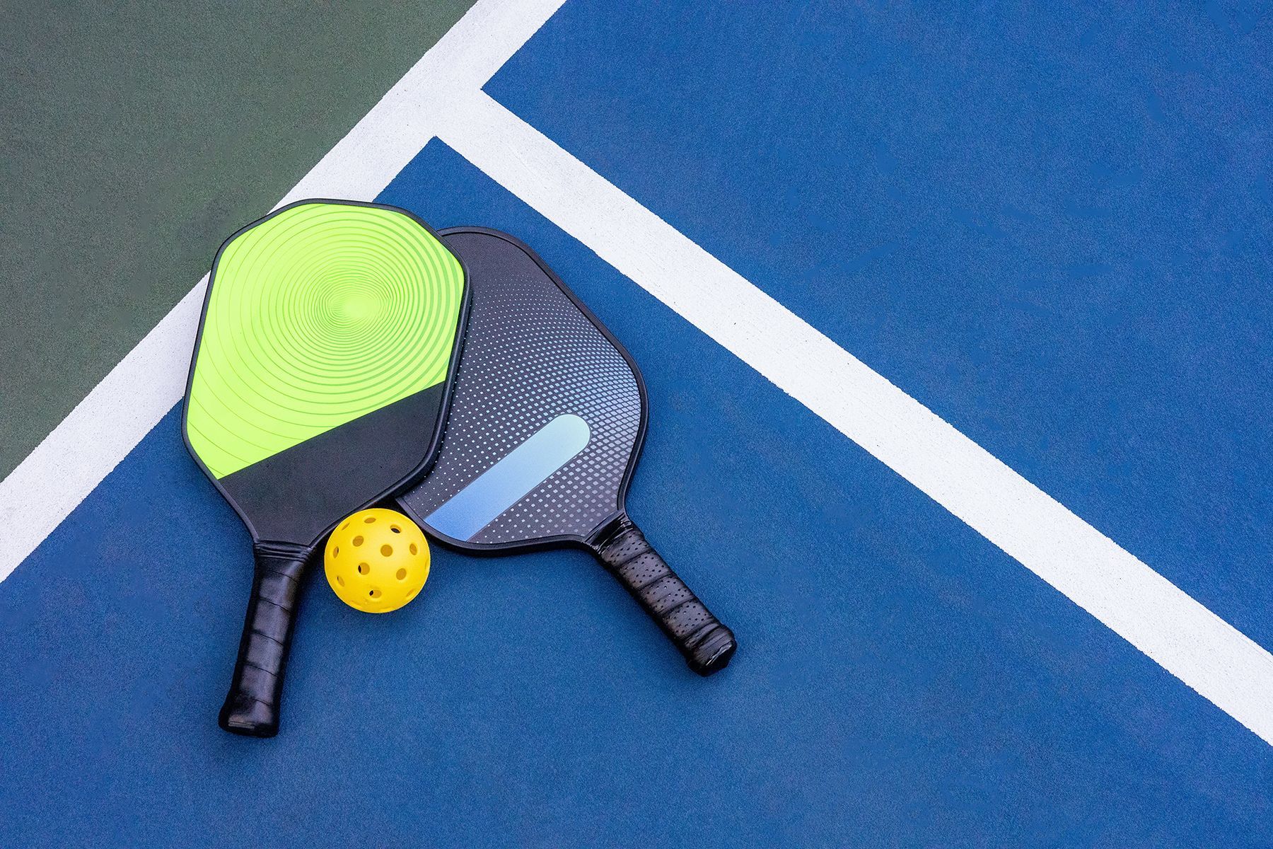 Two pickle ball rackets and a ball on a pickle ball court.
