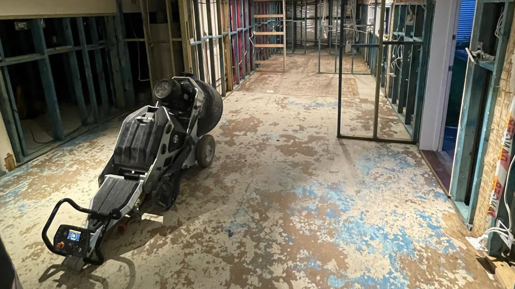 Battered overturned wheelchair in a dilapidated room with exposed framing and peeling paint.