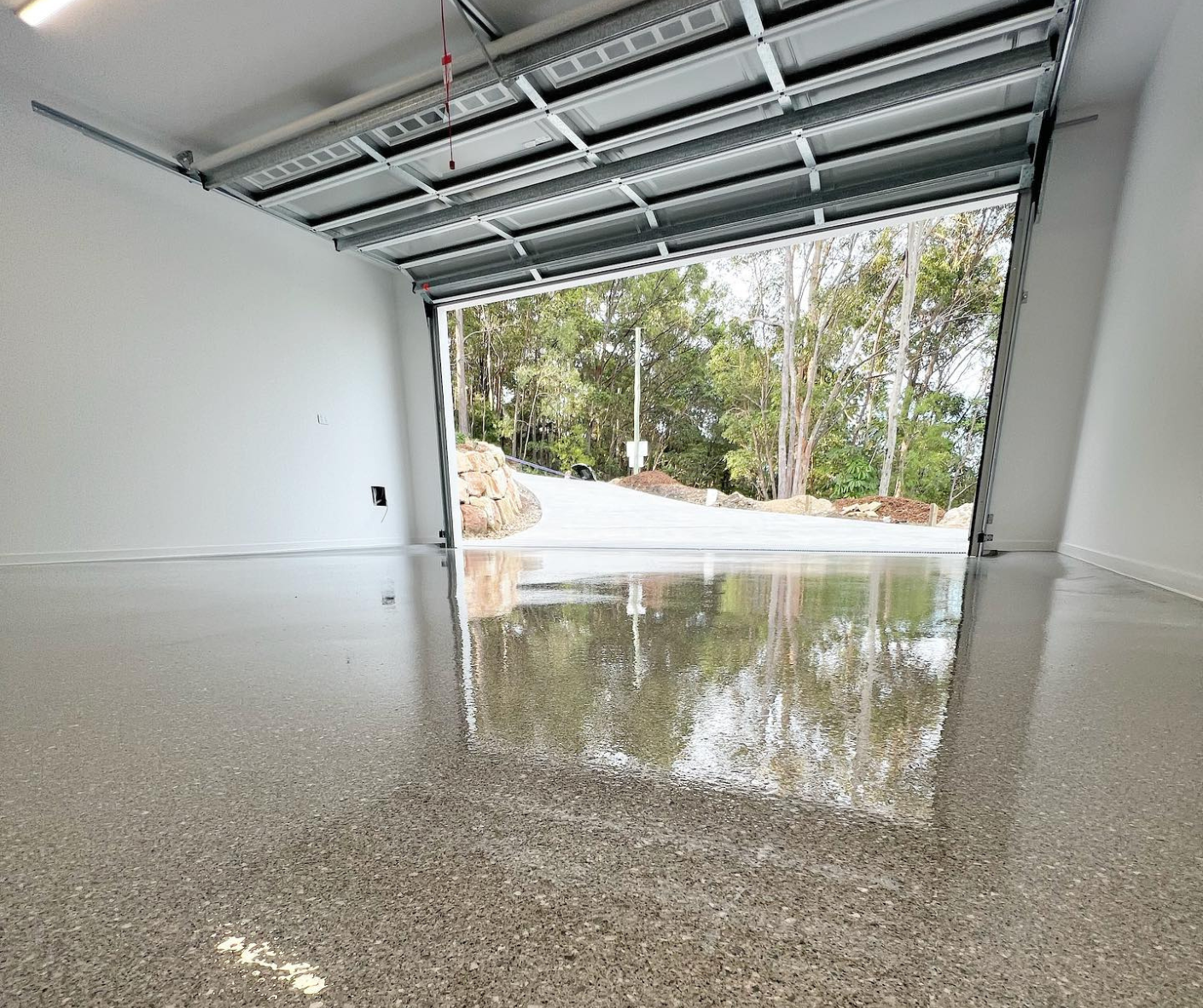 Empty garage with glossy speckled floor reflecting trees outside the open door