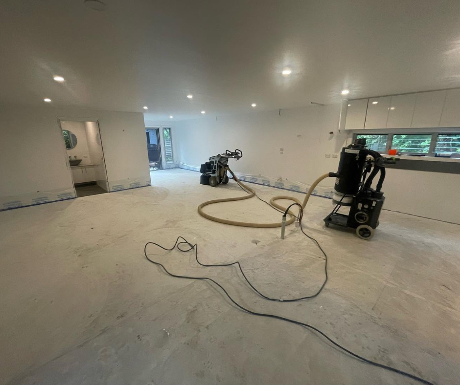 Empty renovated room with two floor sanders and cords on a bare concrete floor