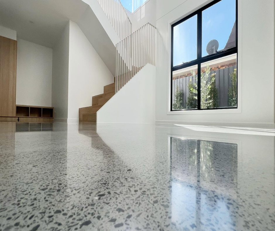 Bright minimalist interior with terrazzo floor, staircase, large window, and reflected sunlight