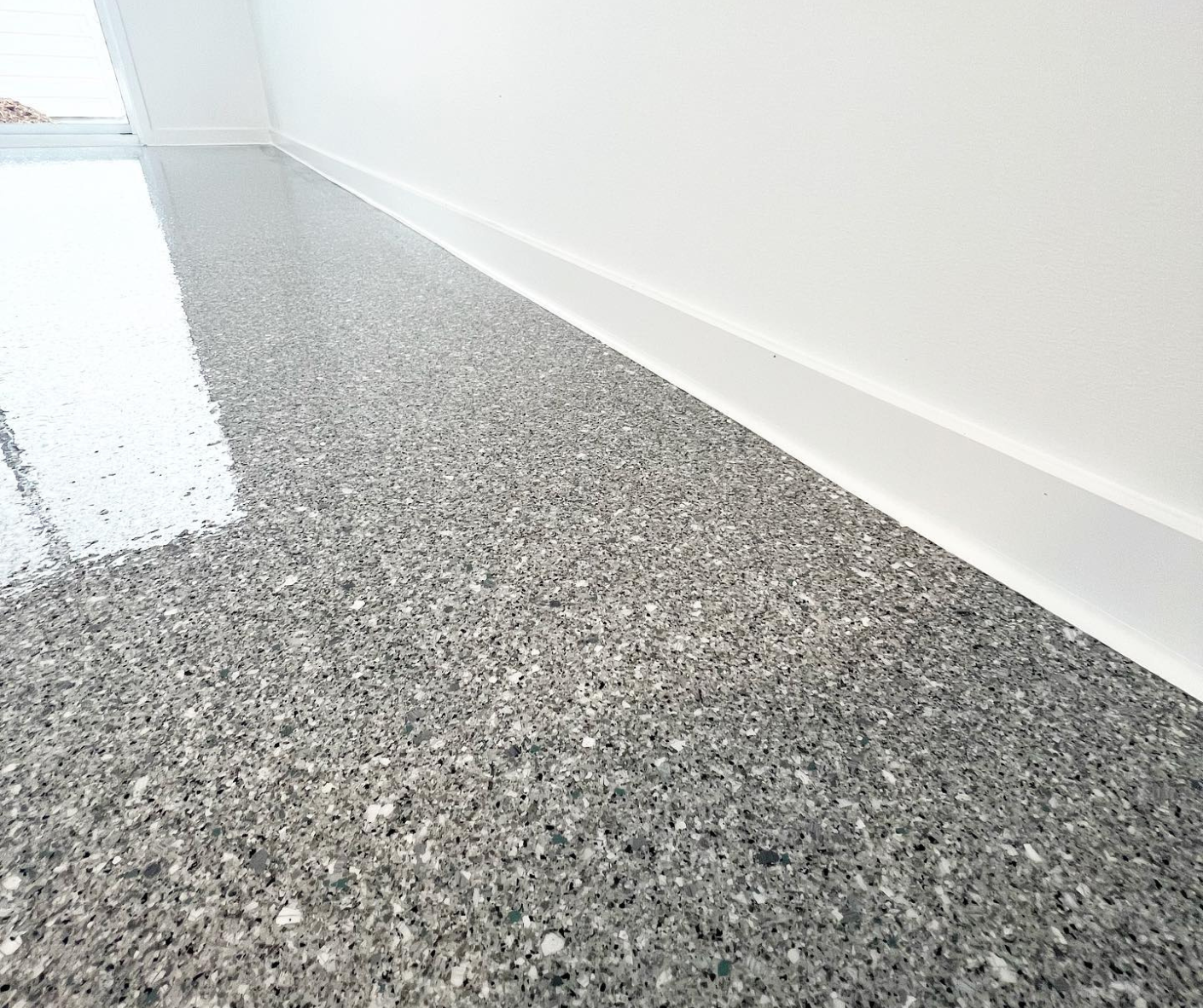 Gray speckled epoxy floor meeting a white wall in a bright, empty room