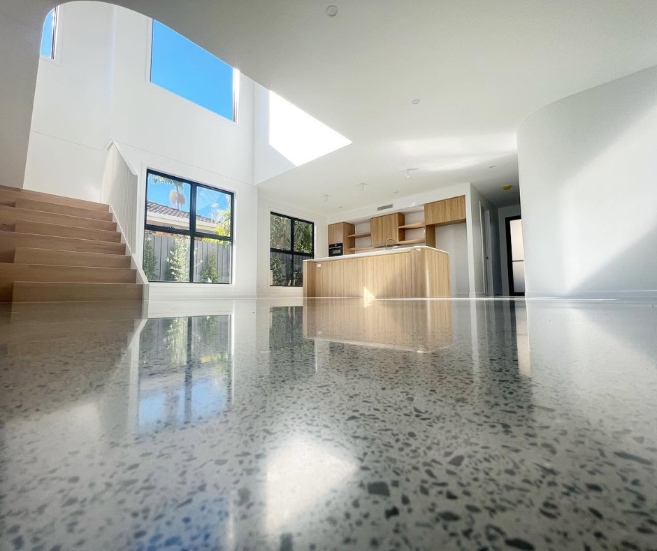 Modern bright open-plan home interior with staircase, kitchen island, and sunlit terrazzo floor Modern bright open-plan home interior with staircase, kitchen island, and sunlit terrazzo floor