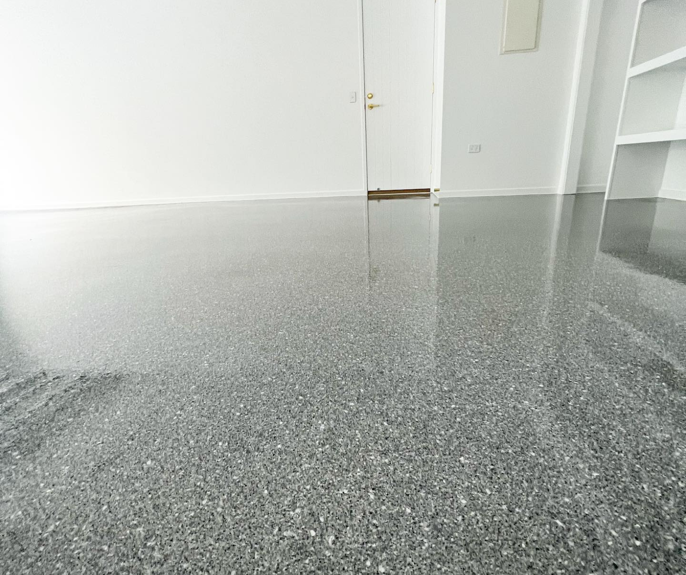 Empty room with gray speckled floor and white walls, viewed from a low angle.