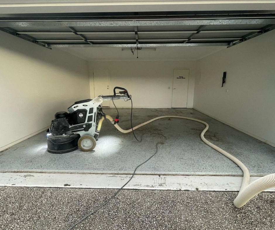 Garage with a floor grinder and hose on a concrete floor under a raised garage door. Garage with a floor grinder and hose on a concrete floor under a raised garage door.