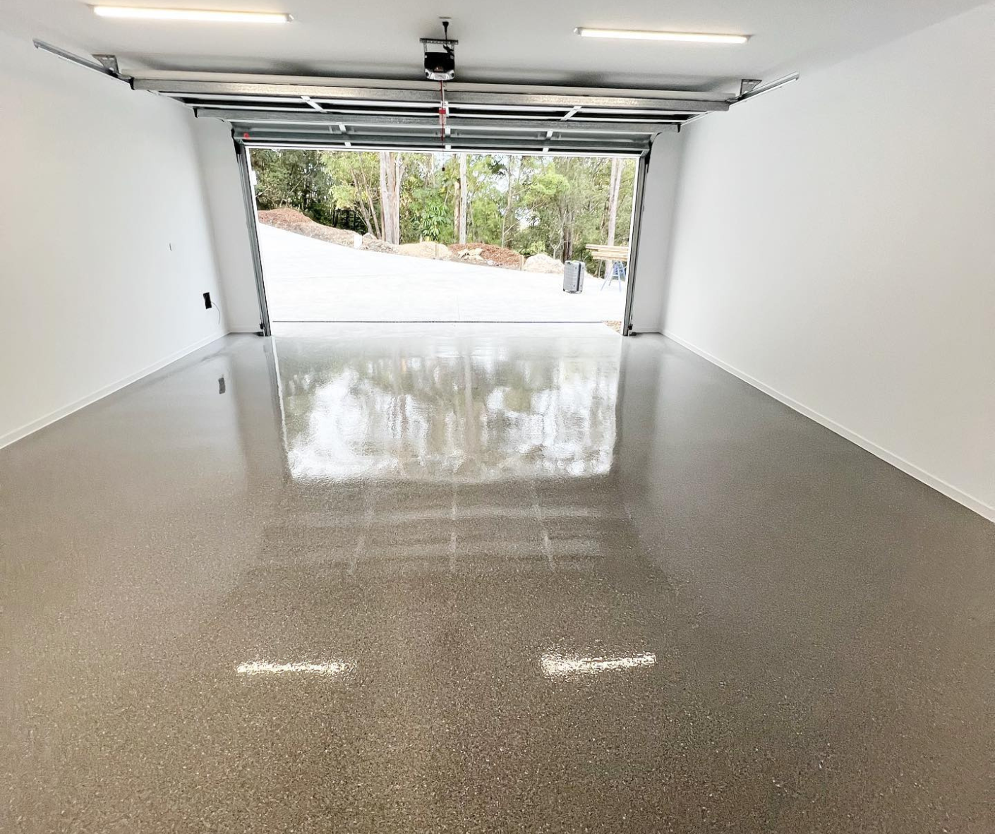 Empty garage with polished concrete floor and open door to a driveway outside