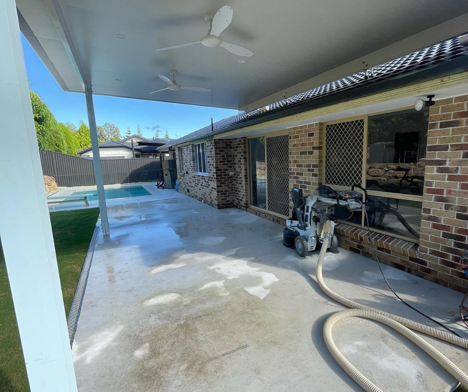 Covered backyard patio with brick house exterior, ceiling fan, and garden hose on a wet concrete floor Covered backyard patio with brick house exterior, ceiling fan, and garden hose on a wet concrete floor