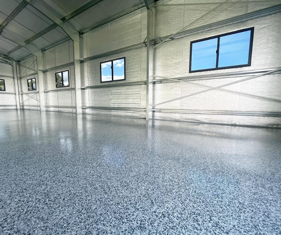Empty industrial warehouse with polished speckled floor and large windows letting in daylight