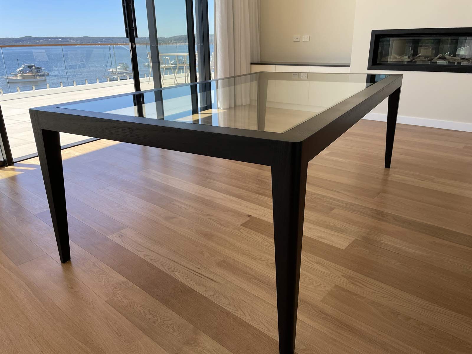 Glass-topped Dining Table With Black Frame on Wooden Floor, Overlooking a Water View — Norrland in Warners Bay, NSW