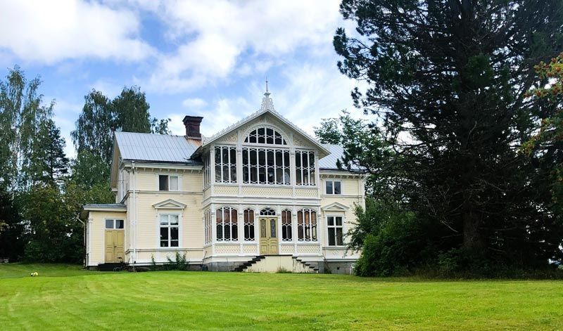 Large, light yellow Victorian house with a green lawn and blue sky.