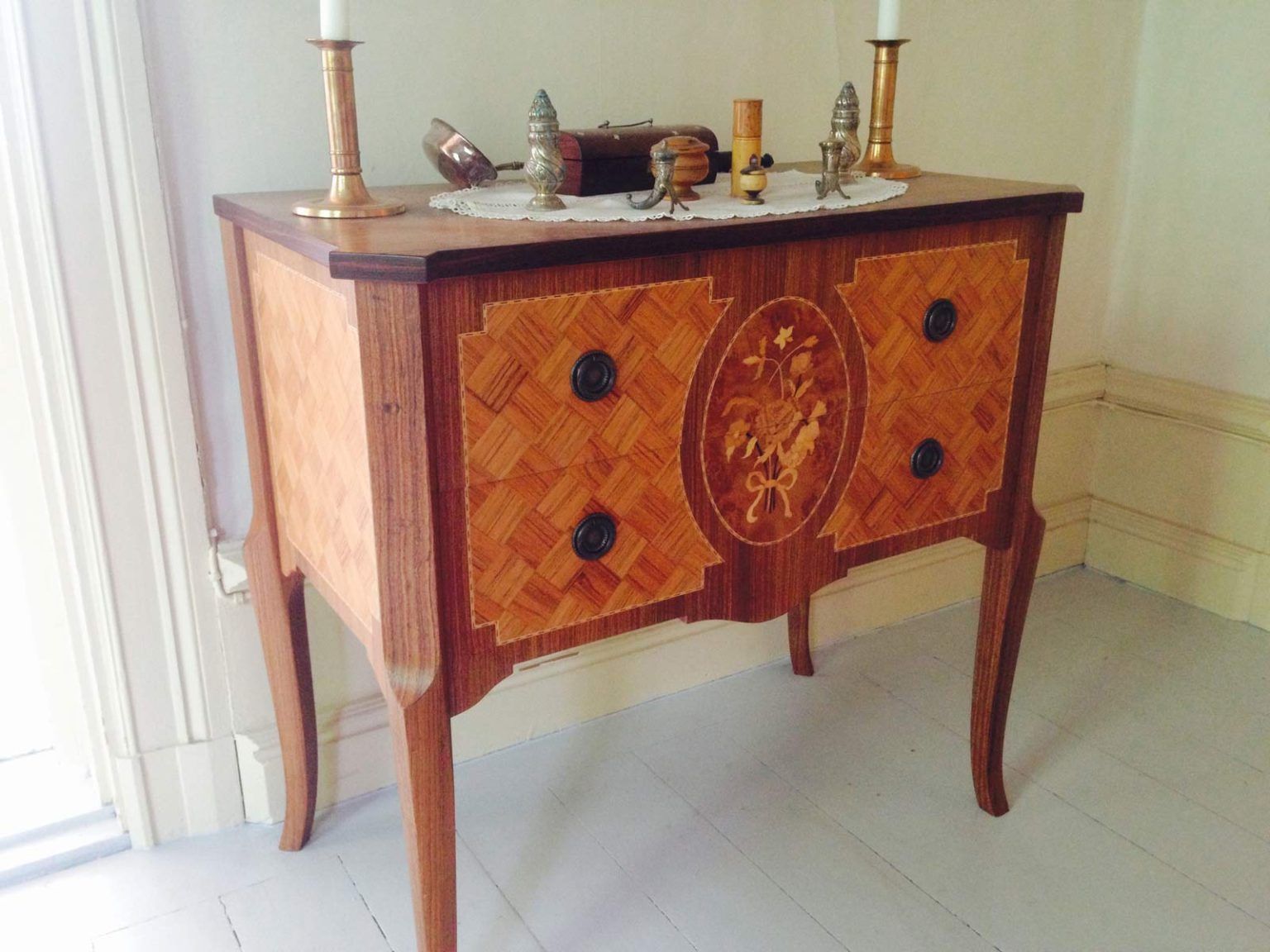 Wooden inlaid side table with four drawers, decorative panel, and candle holders.