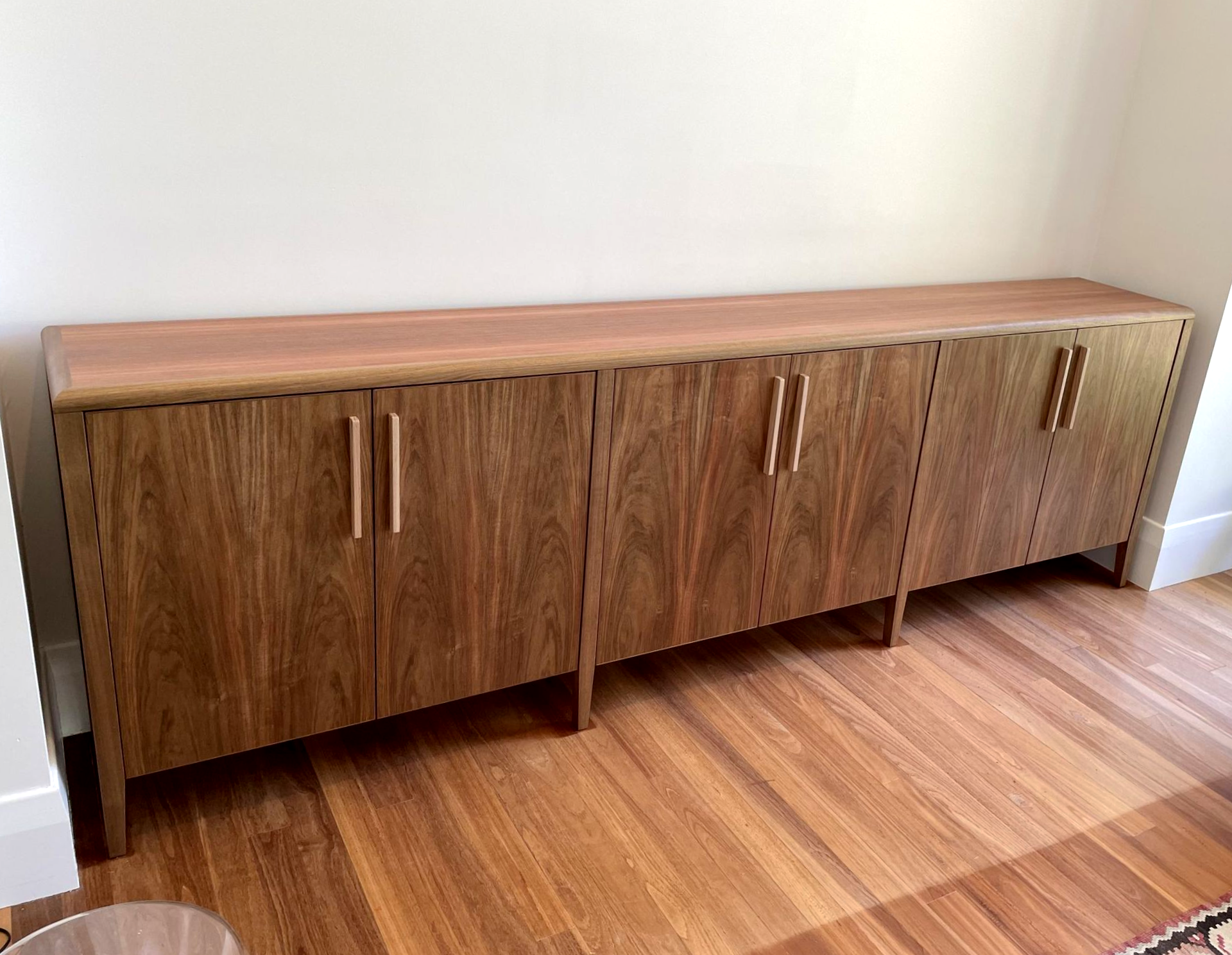 A long, mid-century modern wooden sideboard with vertical grain doors and slender metal handles sits on a wood floor — Norrland in Warners Bay, NSW