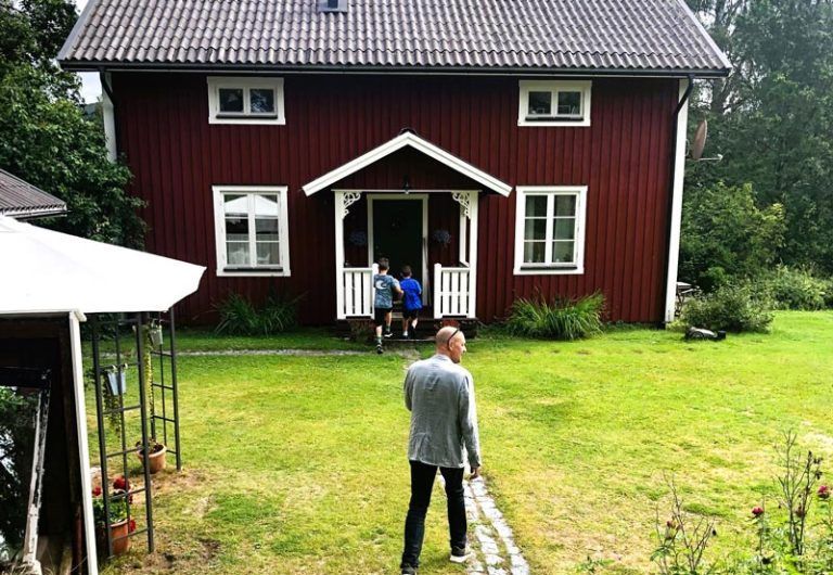 Red house with white trim; person walking towards the entrance where two others are sitting.