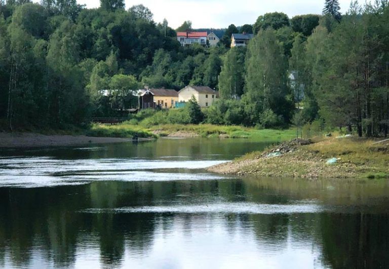 River flowing through a green landscape with buildings on a distant hillside.