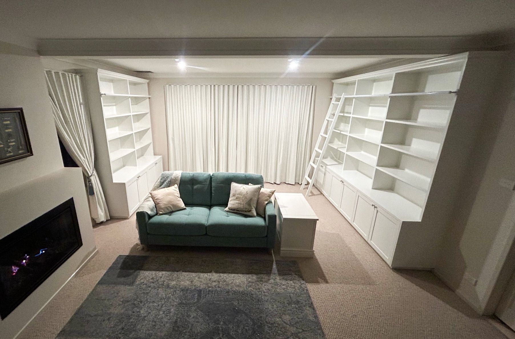 Living Room With Built-in White Bookshelves, a Teal Sofa, Fireplace, Curtains, and a Blue Rug — Norrland in Warners Bay, NSW