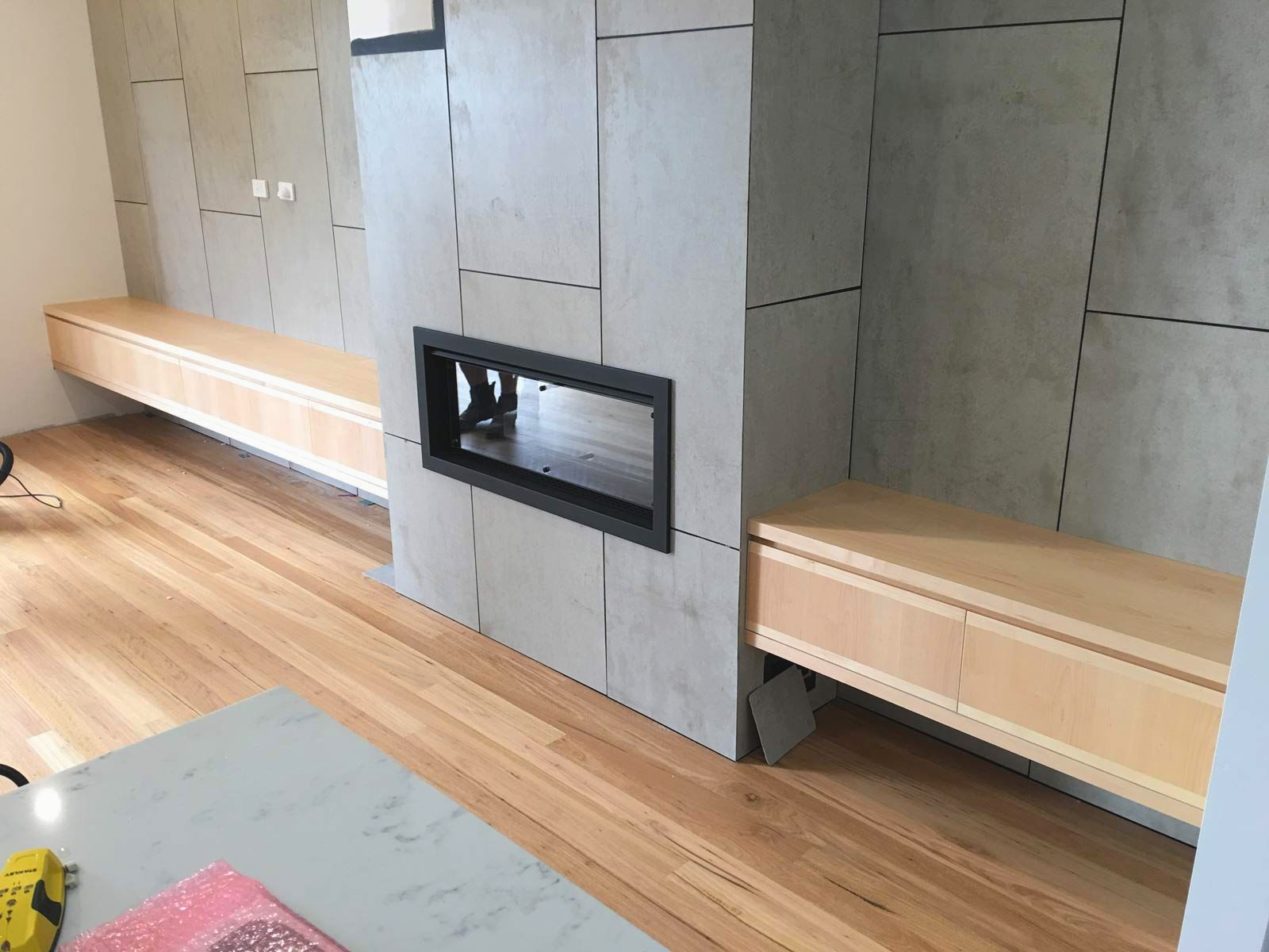 Modern living room with a linear fireplace set in a gray paneled wall, flanked by light wood floating storage cabinets — Norrland in Warners Bay, NSW