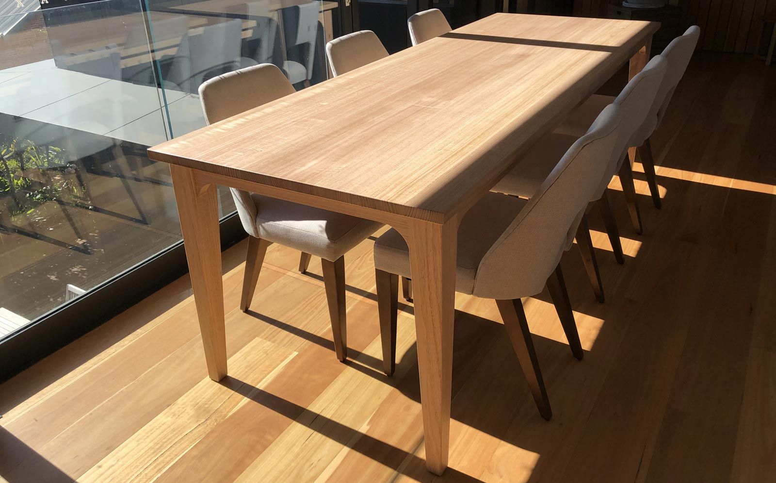 A light wood dining table with chairs arranged around it in a room with hardwood floors and large glass windows — Norrland in Warners Bay, NSW