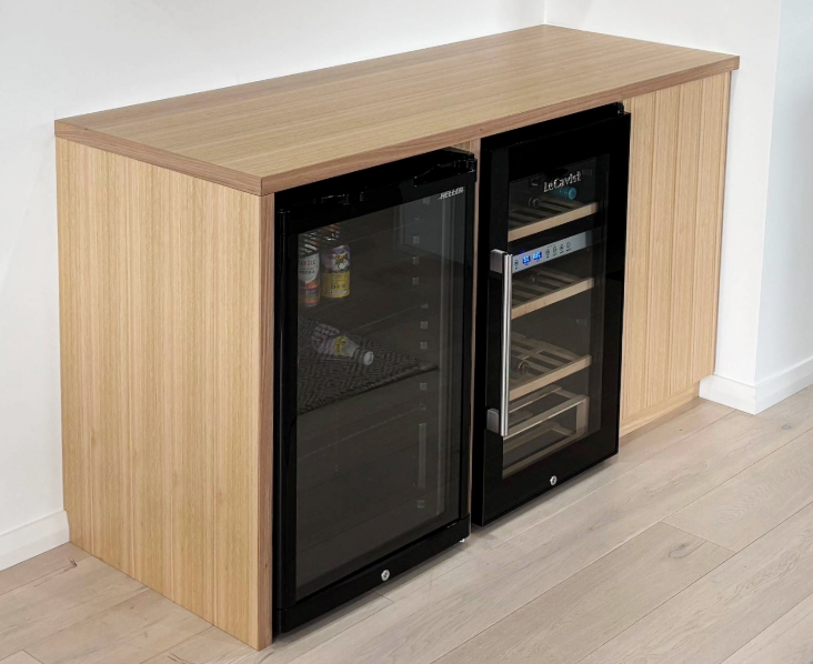 Wood-finish beverage fridge cabinet with two black glass-front mini fridges against a white wall