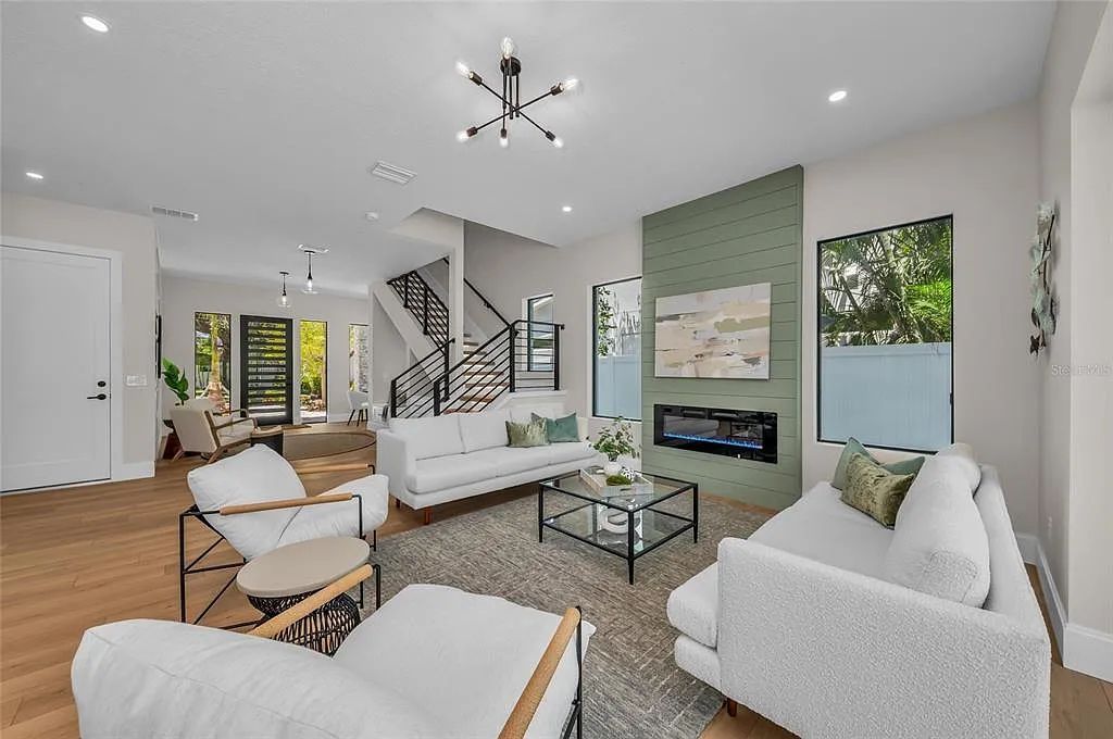 Bright modern living room with white sofas, fireplace, staircase, wood floor, and large windows