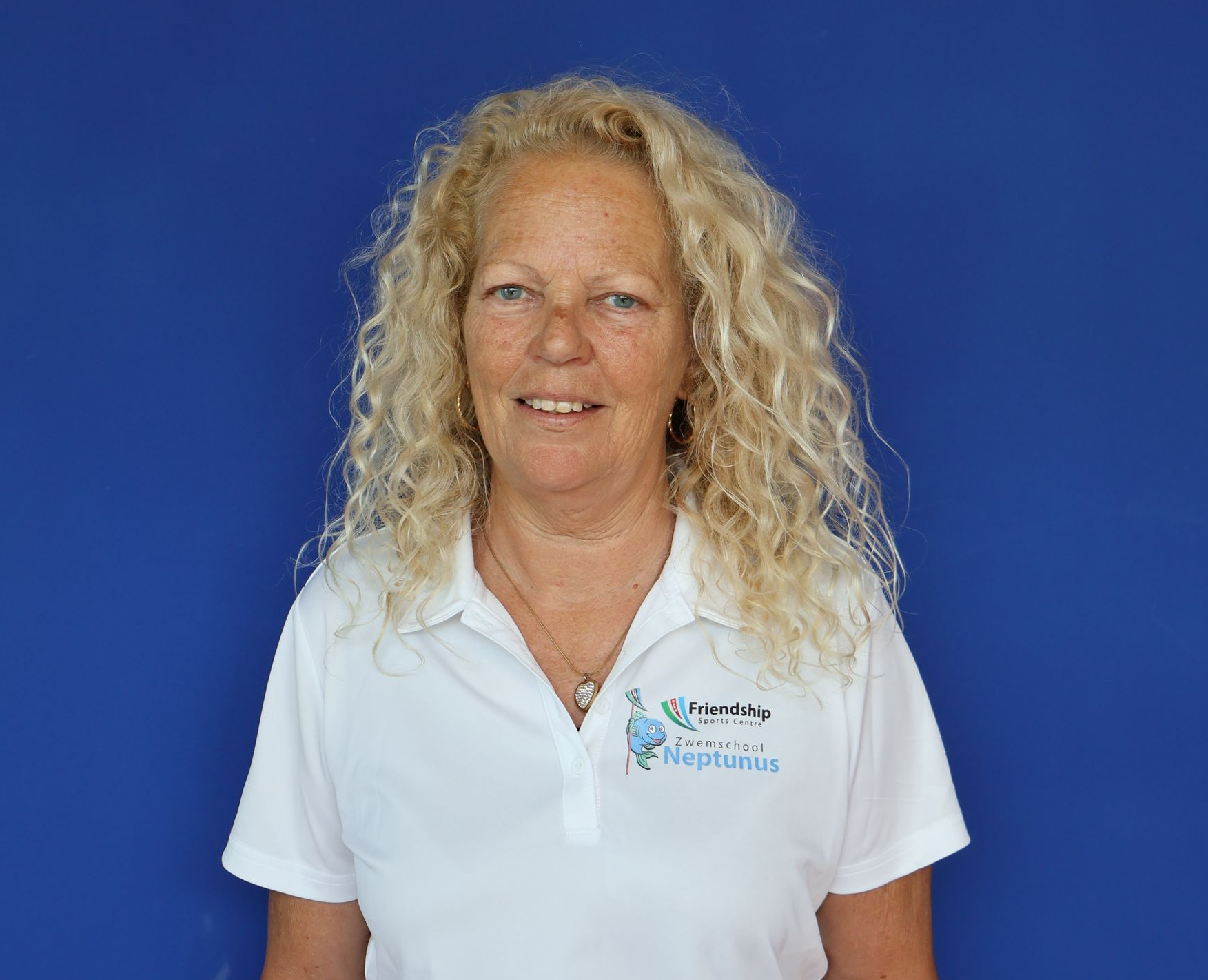 Vrouw met krullend blond haar, gekleed in een witte poloshirt, tegen een blauwe achtergrond.