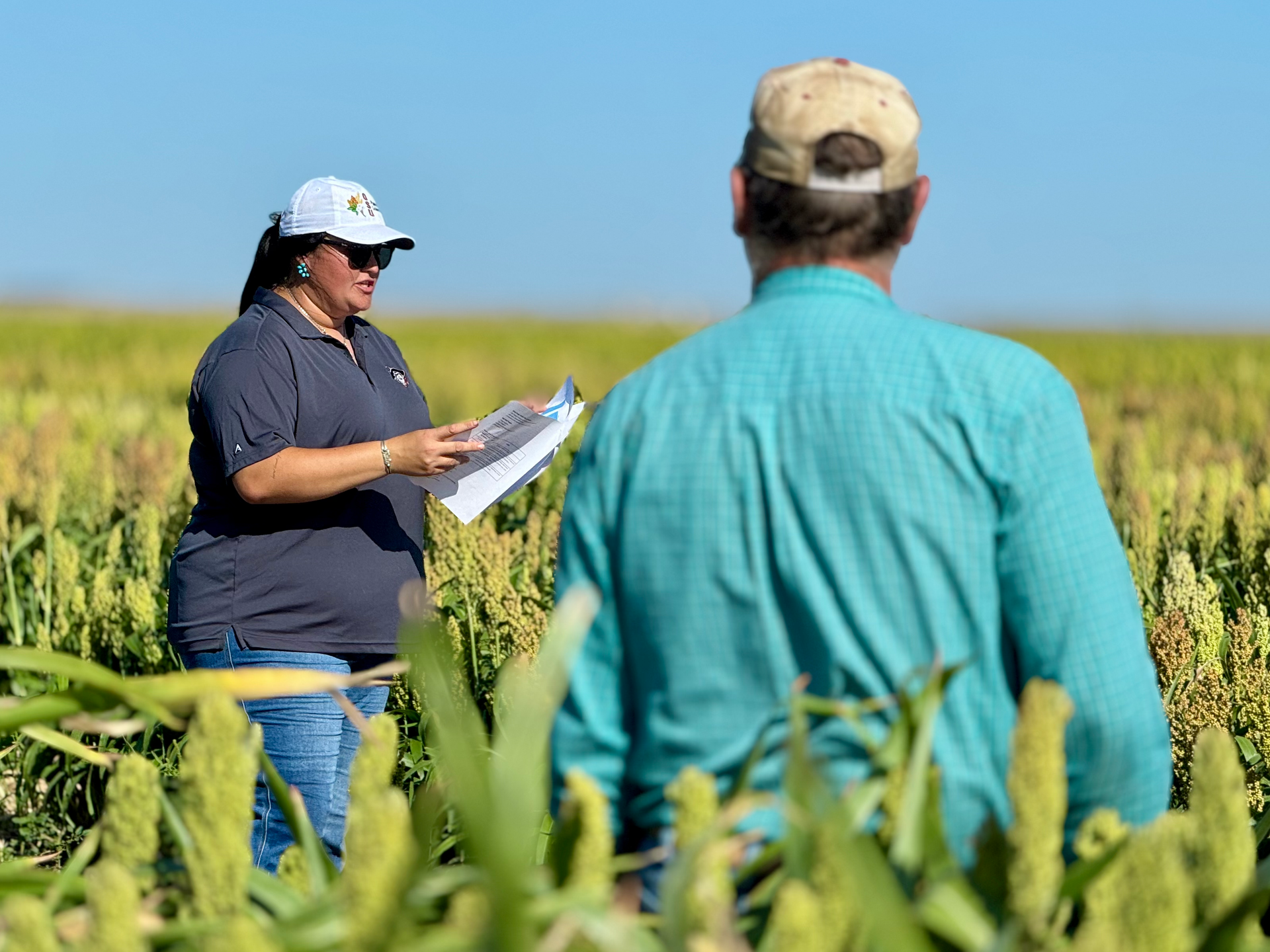 A man and a woman are standing in a field and the woman is holding a clipboard