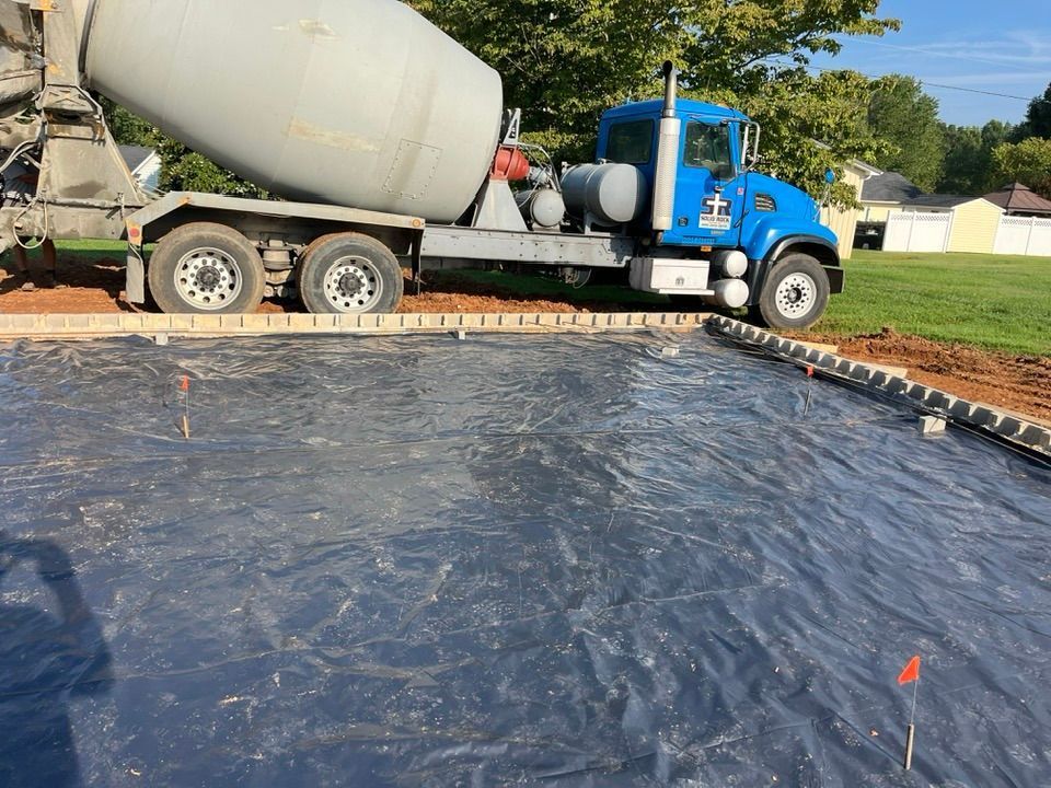 A blue concrete mixer truck parked next to a construction site area covered with a large black plastic vapor barrier.