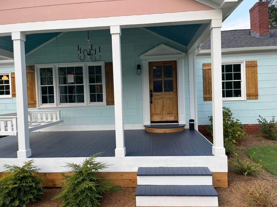 A light blue house with a covered porch, white columns, a natural wood front door, and dark grey porch flooring and steps.