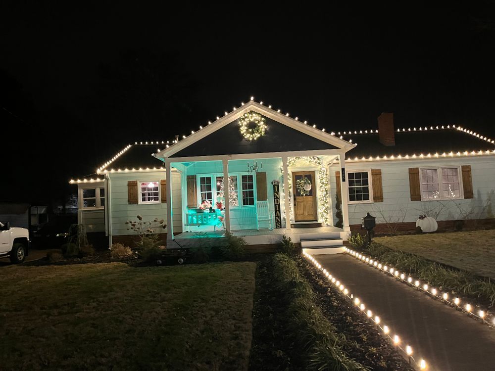 A light-blue house at night, decorated with white string lights and a glowing wreath above the front porch.
