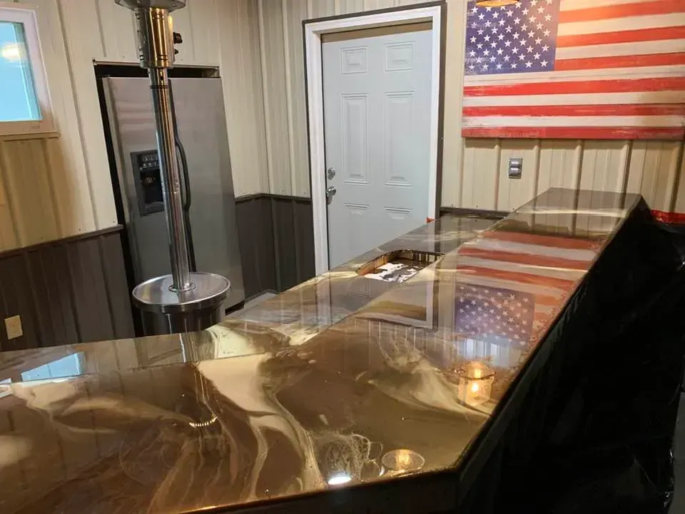 A polished, marbled epoxy bar top in a rustic room featuring a stainless steel refrigerator and an American flag wall art.