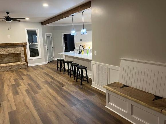 An interior room with board and batten walls painted light gray, wood-look flooring, two windows, and a ceiling fan.