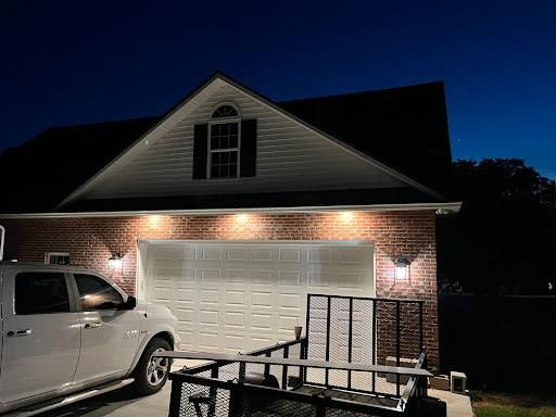 A white pickup truck parked in front of a brick garage at dusk with exterior lights illuminating the house.
