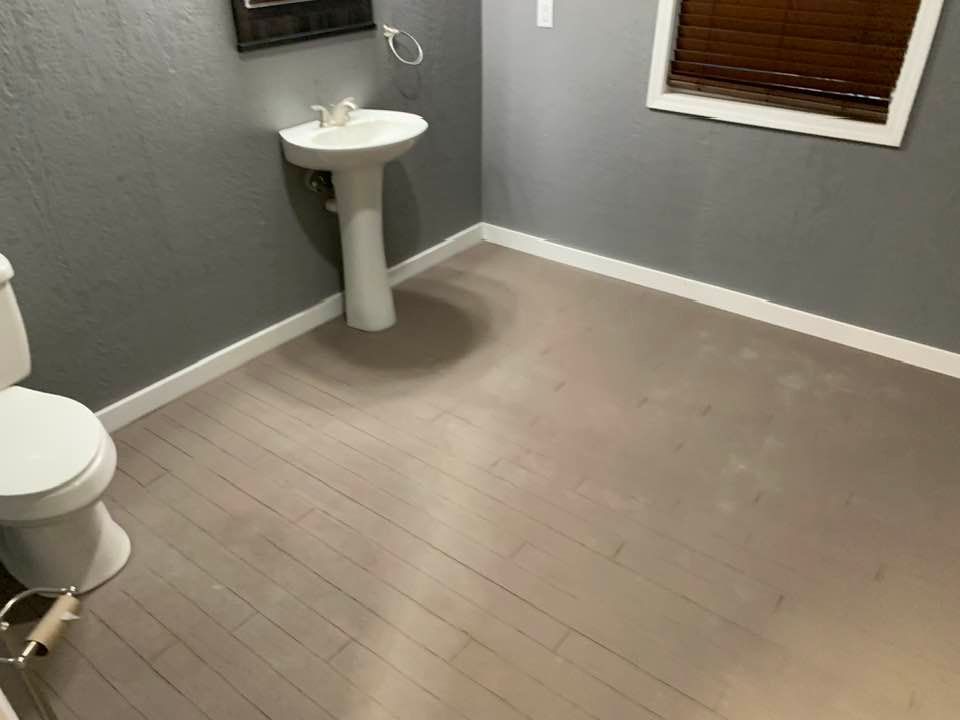 A bathroom with grey walls, a white pedestal sink, a white toilet, and light-colored wood-look flooring.