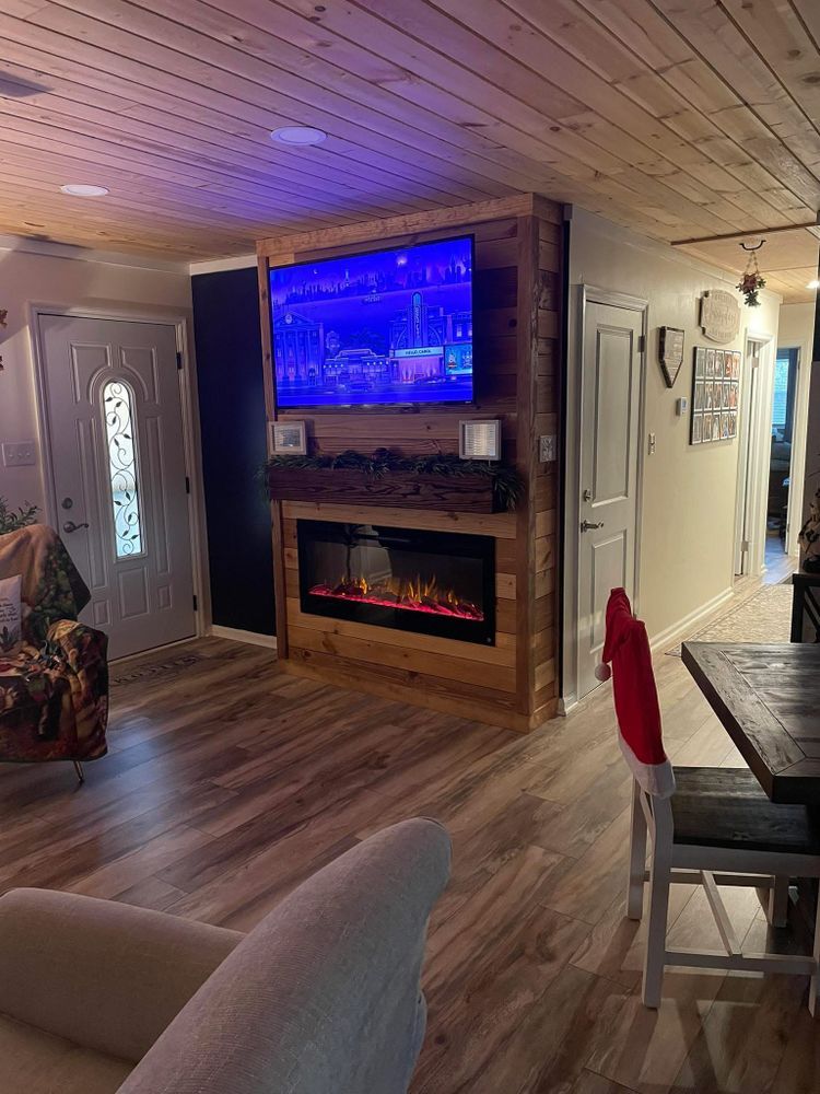 A living room with wood-paneled ceilings, a fireplace and mounted TV on a wood accent wall, and a dining table with chairs.