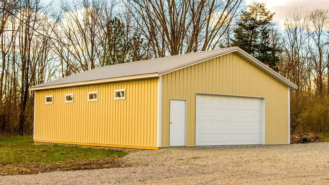 A yellow metal building with a white garage door, a single pedestrian door, and four small windows, set on a gravel lot.